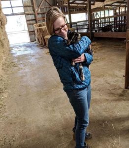 Cheesemonger Ashley on the farm in the stable while holding a baby goat.