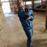 Cheesemonger Ashley on the farm in the stable while holding a baby goat.