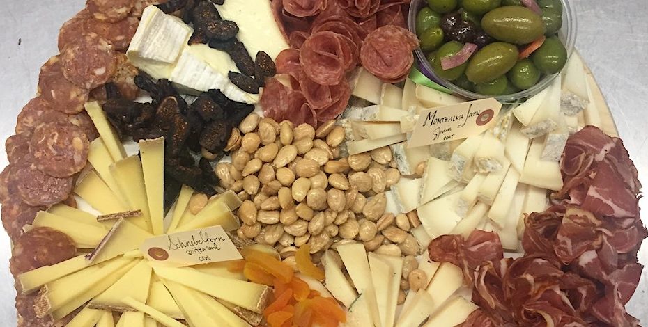 Photo of a cheese platter which includes several different cheeses and meats which have been cut and arranged with artistic style.