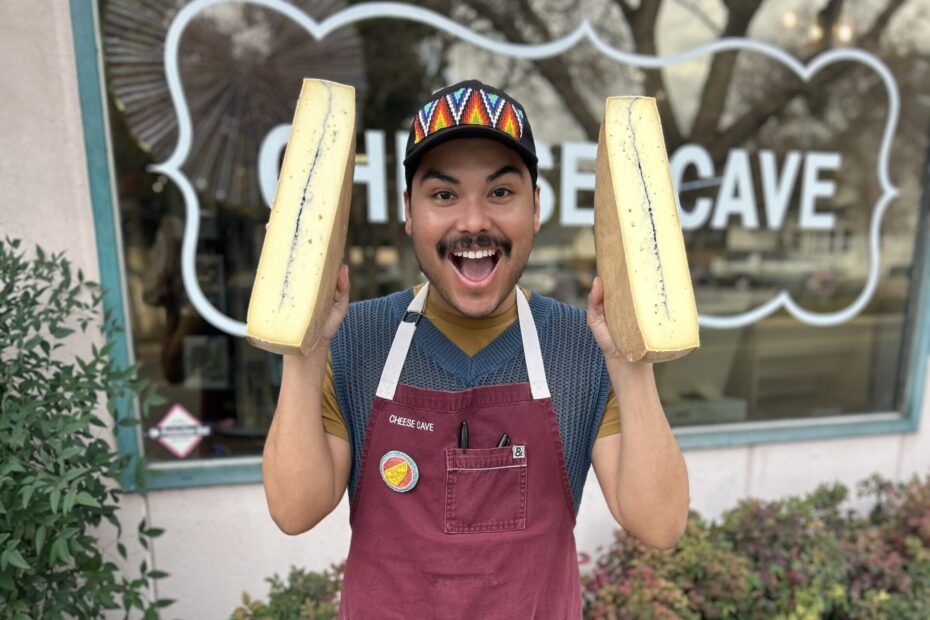 Jacobe standing in front of Cheese Cave holding a large piece of cheese.